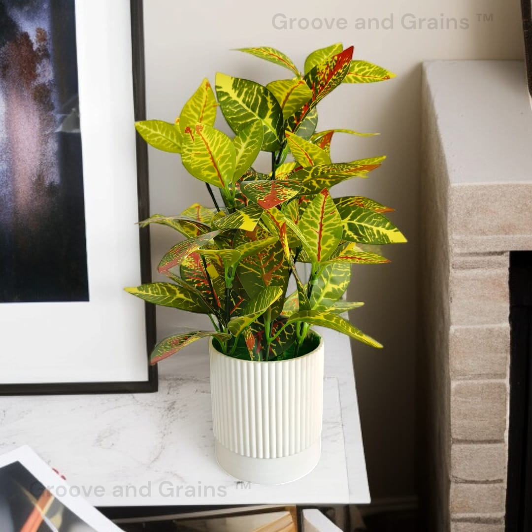 Artificial Croton plant with colorful green, yellow, and red variegated leaves in a white ribbed PVC pot.