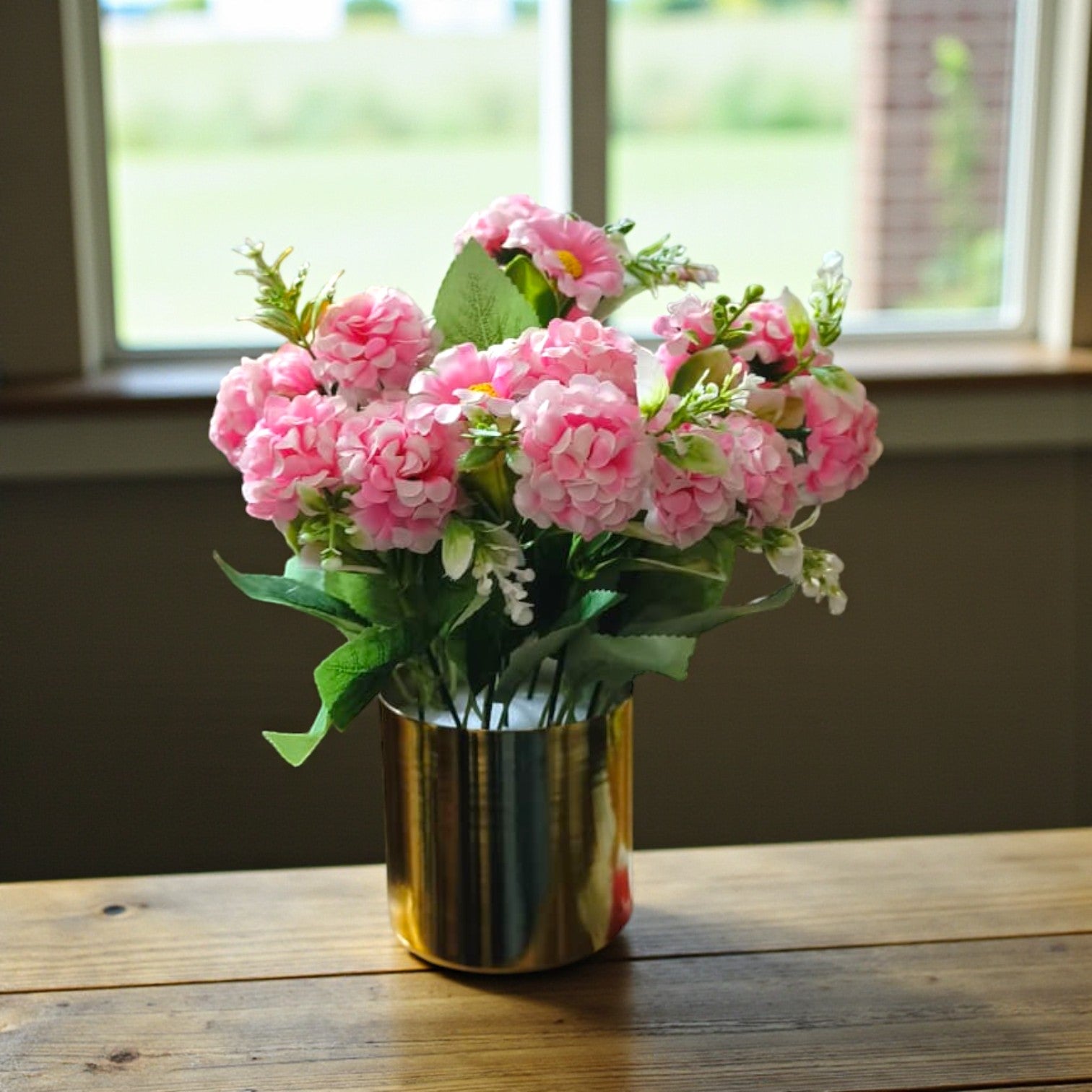 Artificial pink carnation flowers arranged in a cylindrical gold metal pot.