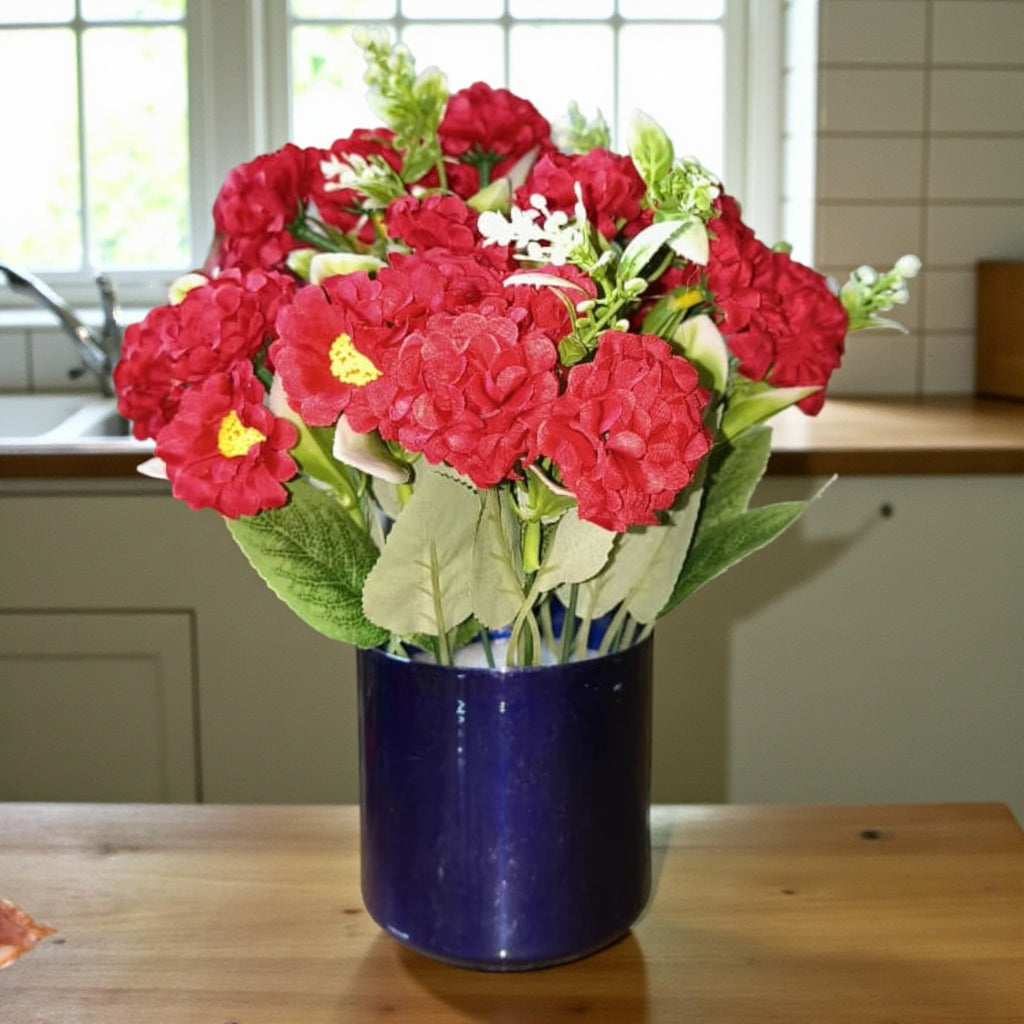 Artificial red carnation flowers in a cylindrical deep blue metal pot.